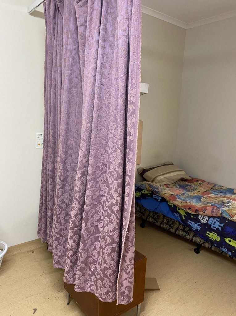 A single bed with robot bedsheets sits in a room, hanging to one side is a purple curtain on a hospital-style curtain rail.