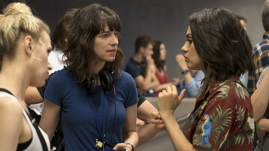 Colour photograph of director Susanna Fogel speaking to actors Mila Kunis and Kate McKinnon on set.