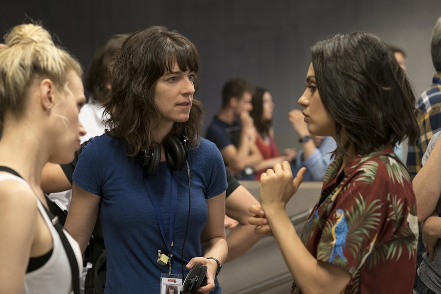 Colour photograph of director Susanna Fogel speaking to actors Mila Kunis and Kate McKinnon on set.