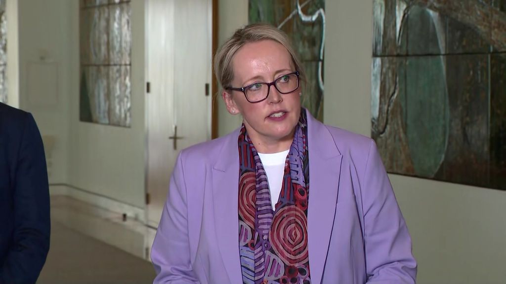 A woman in a purple jacket looks off camera during a press conference