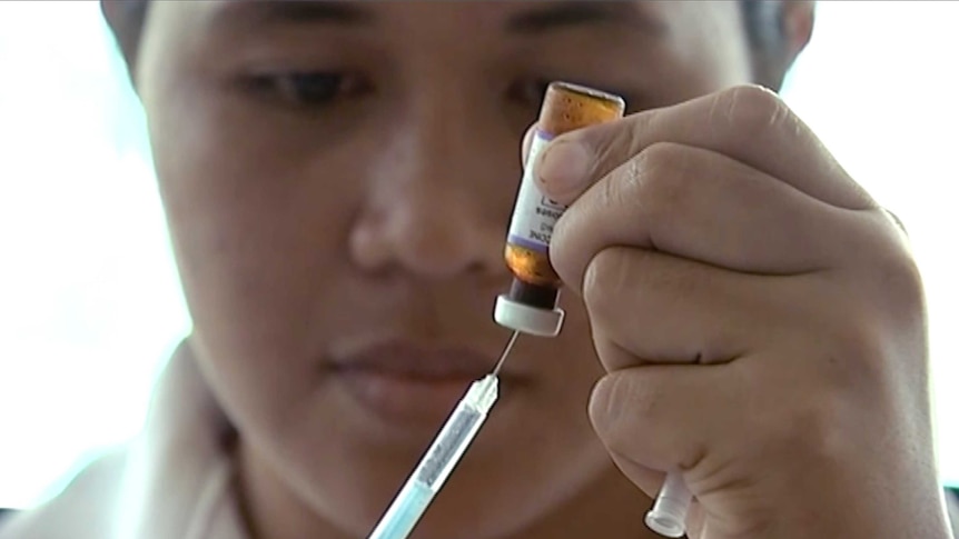 A New Zealand health official prepares a measles vaccination at a clinic, putting a syringe into a small bottle.