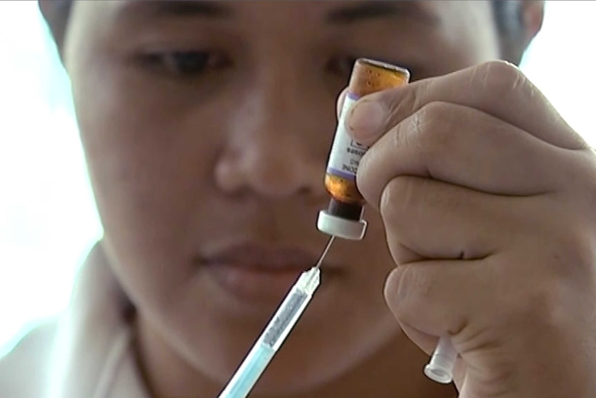 A New Zealand health official prepares a measles vaccination at a clinic, putting a syringe into a small bottle.