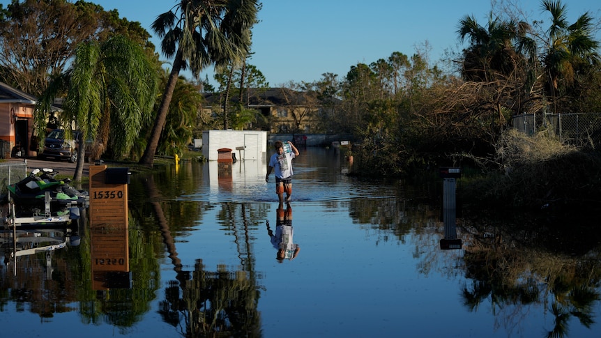 A man carries items recovered from his family's waterlogged car through receding flood waters.