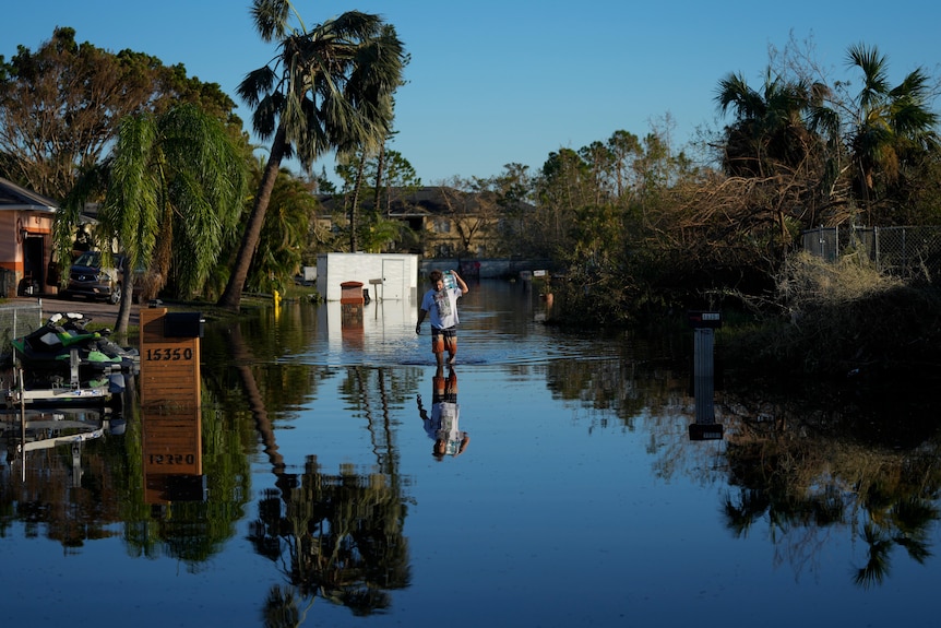 A man carries items recovered from his family's waterlogged car through receding flood waters.