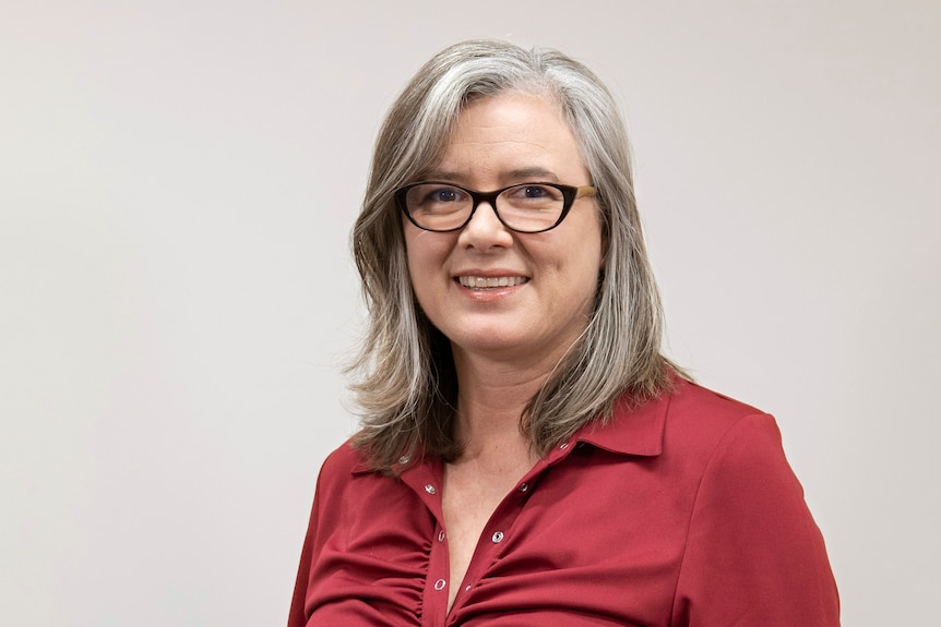A grey hair woman with red shirt and glasses, a headshot. She's smiling.