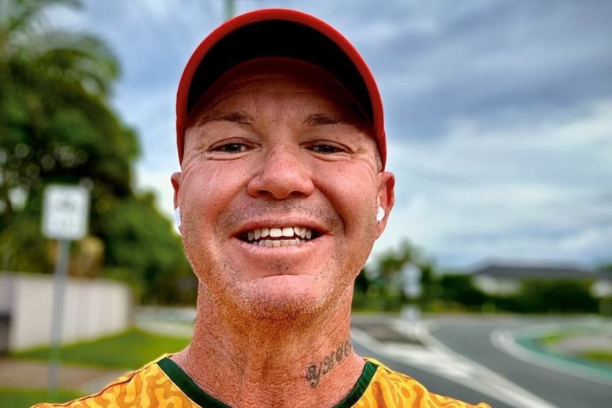 A smiling, middle-aged man in a cap takes a selfie on a suburban street.