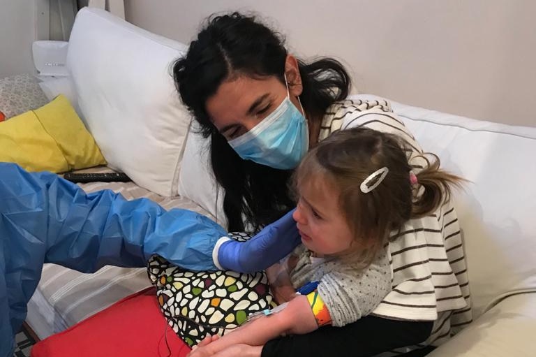 Camilla sits on Francesca's knee as a nurse takes blood.