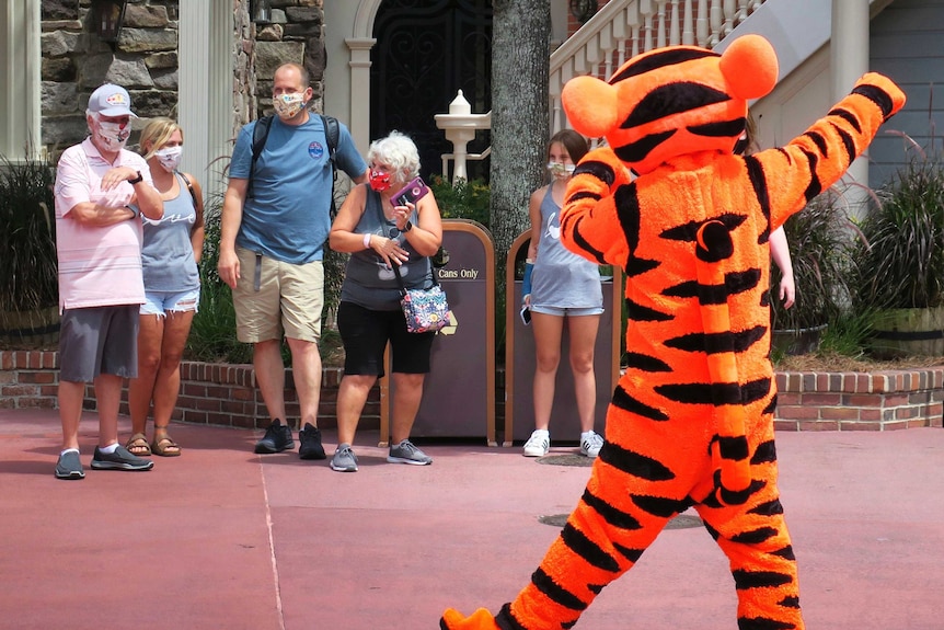 A performer in a Tigger costume waves at people wearing masks at Disney World.