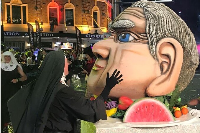 A person dressed as a nun puts their hand on the cheek of a statue of Fred Nile's head.