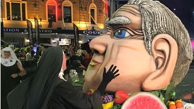 A person dressed as a nun puts their hand on the cheek of a statue of Fred Nile's head.