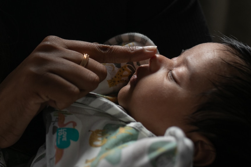 A close up of a sleeping baby with hair as a woman's hand with a gold ring touches the baby's nose.