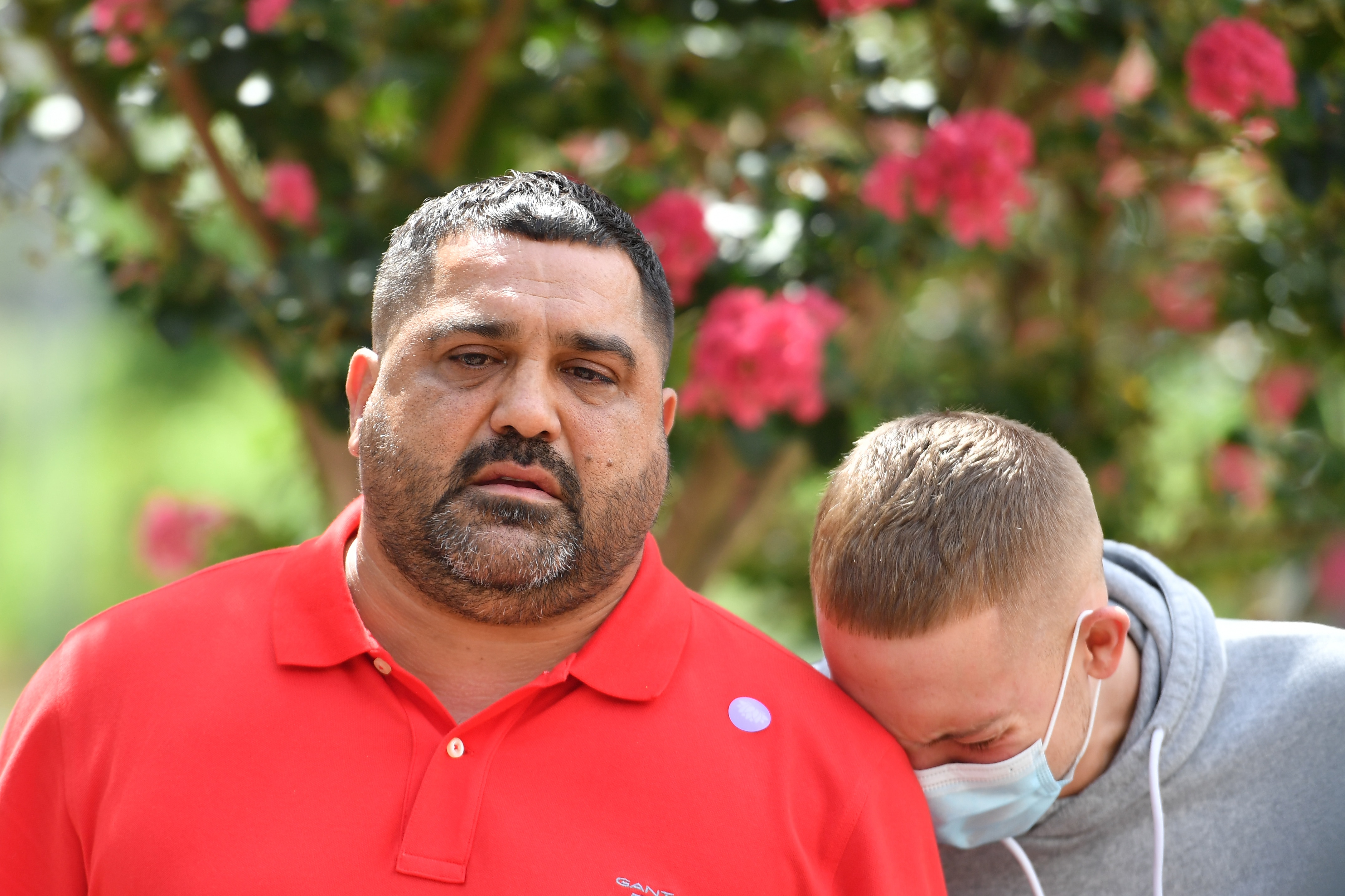 A man with dark hair and a red shirt with tears. a boy with a grey jumper cries next to him