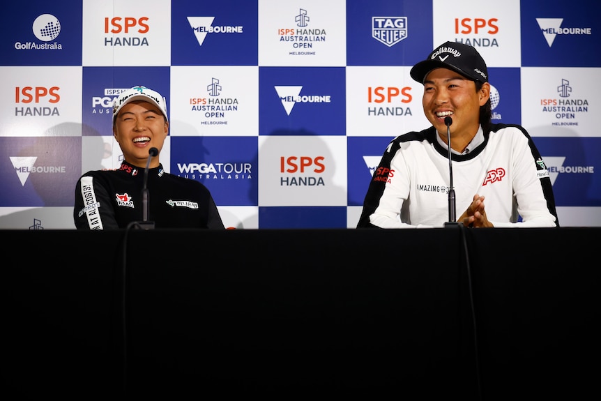 Man and woman look happy sitting at press conference desk with logo-emblazoned board behind them