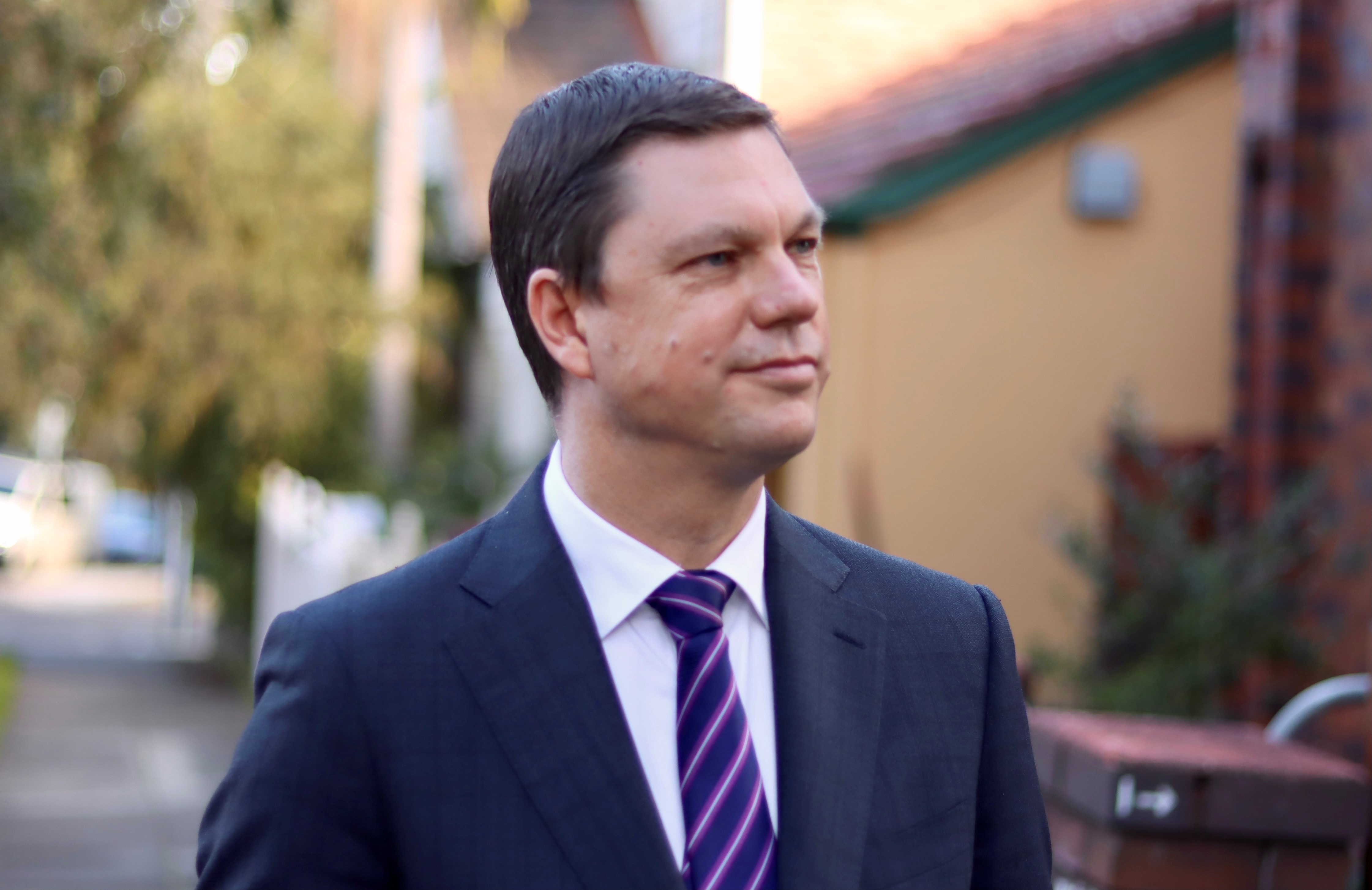 Ken Morrison in a blue suit looking down the street near his home in Sydney