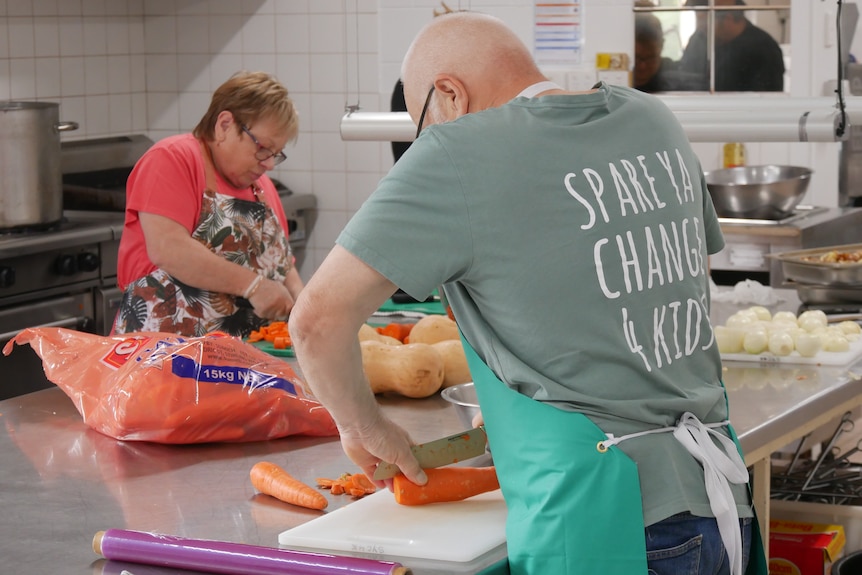A person chopping carrots with their back to camera. Their shirt says spare your change for kids. 