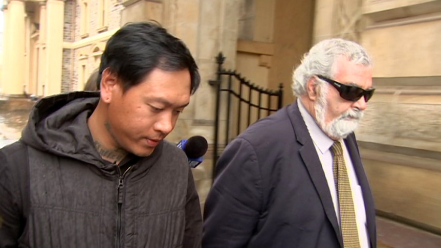 Two men walk outside a stone building.