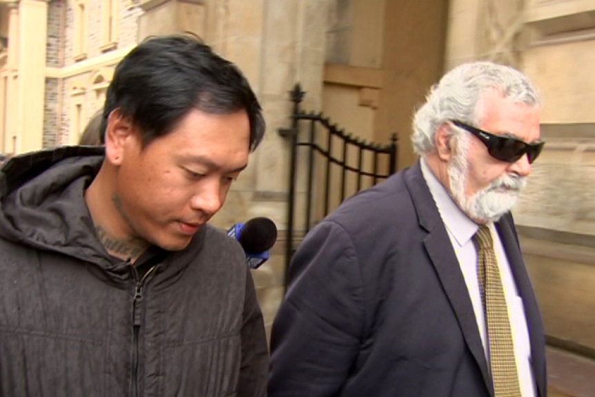 Two men walk outside a stone building.