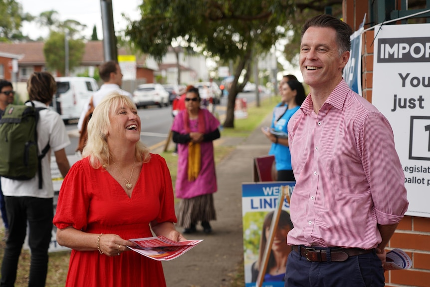 A woman in a red dress and a man in a pink shirt at a polling booth