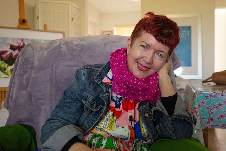 Woman with short red hair sits on a couch leaning on her hand  