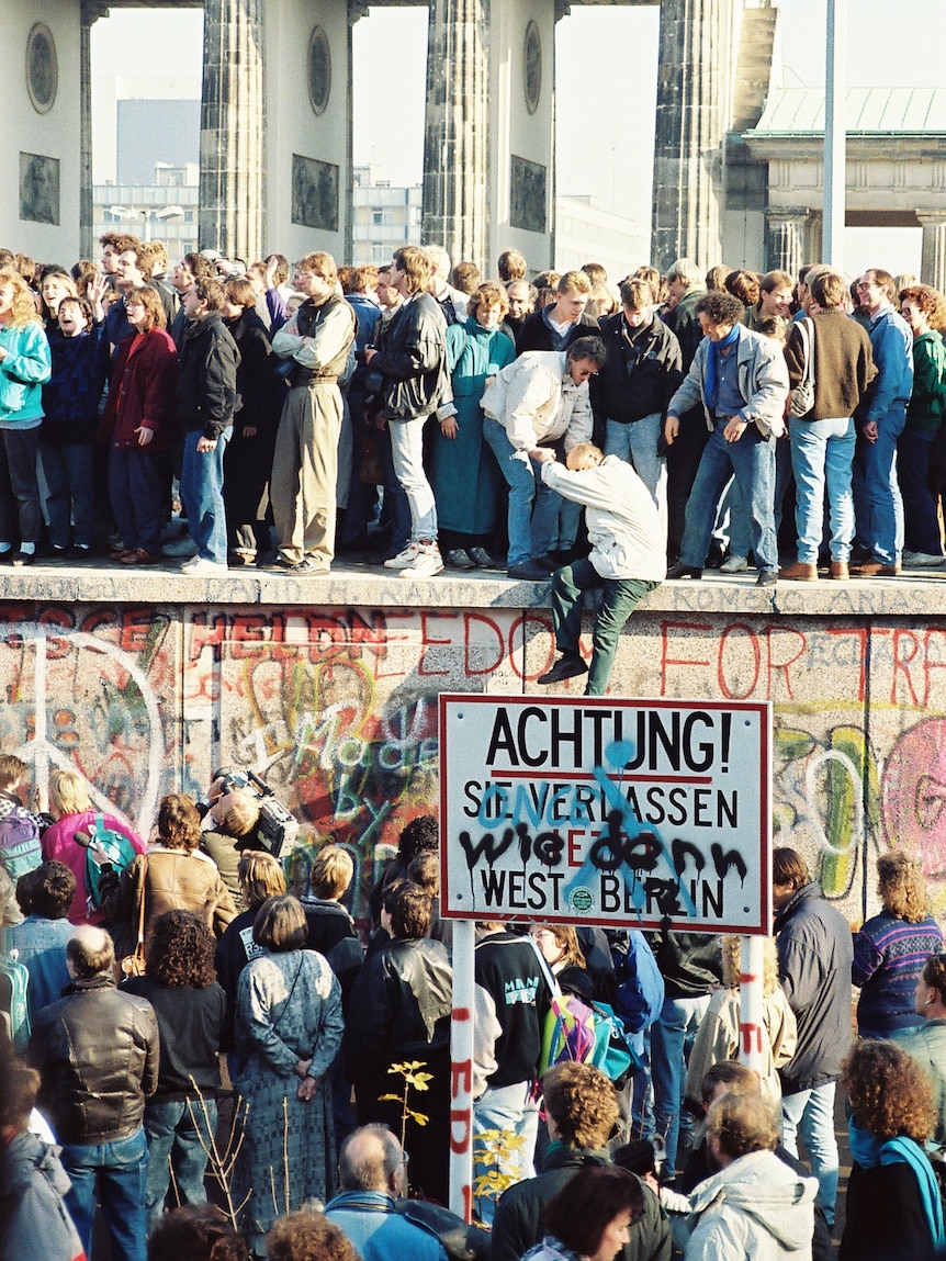 A photo from 1989 showing a huge crowd of people standing on the Berlin Wall, helping people below get up