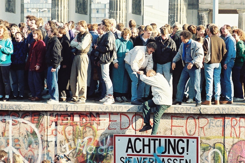 A photo from 1989 showing a huge crowd of people standing on the Berlin Wall, helping people below get up
