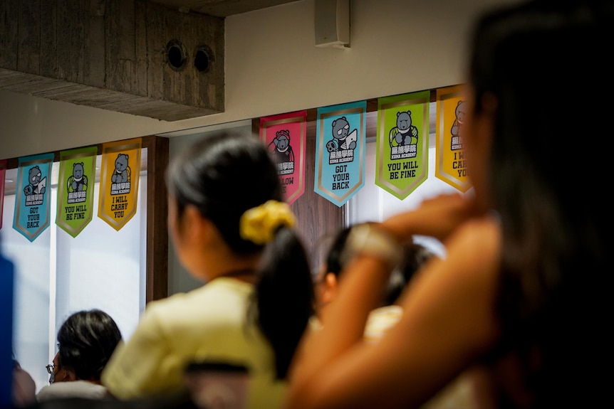 Colourful flags line the windows of a classroom, with bears and messages saying YOU WILL BE FINE