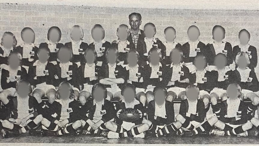 A large group of boys in Australian rules strips pose for a photo with their coach.