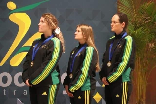 Three women wearing Australian black, gold and green jumpsuits wearing medals