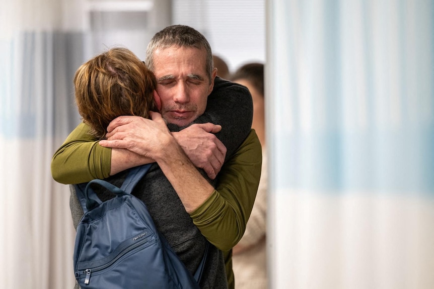 Fernando Simon Marman hugs a woman around the same age with short hair tightly in a hospital hallway