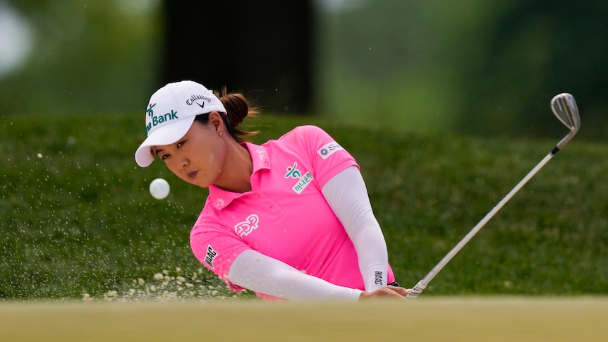 Australian golfer Minjee Lee, wearing a pink top, hits her ball out of a bunker