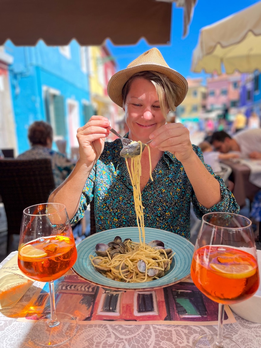 A lady eating a shell pasta with a smile and a hat on 