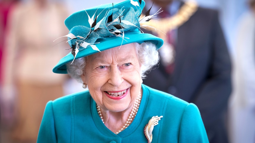 Queen Elizabeth smiles at the camera in a blue blazer and hat, July 1, 2021.