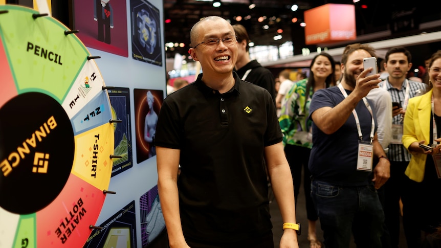 A man stands smiling next to a brightly coloured spinning wheel with Binance written on it. 