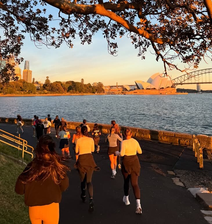 A group of women run with the Sydney Harbour bridge and Opera House in view