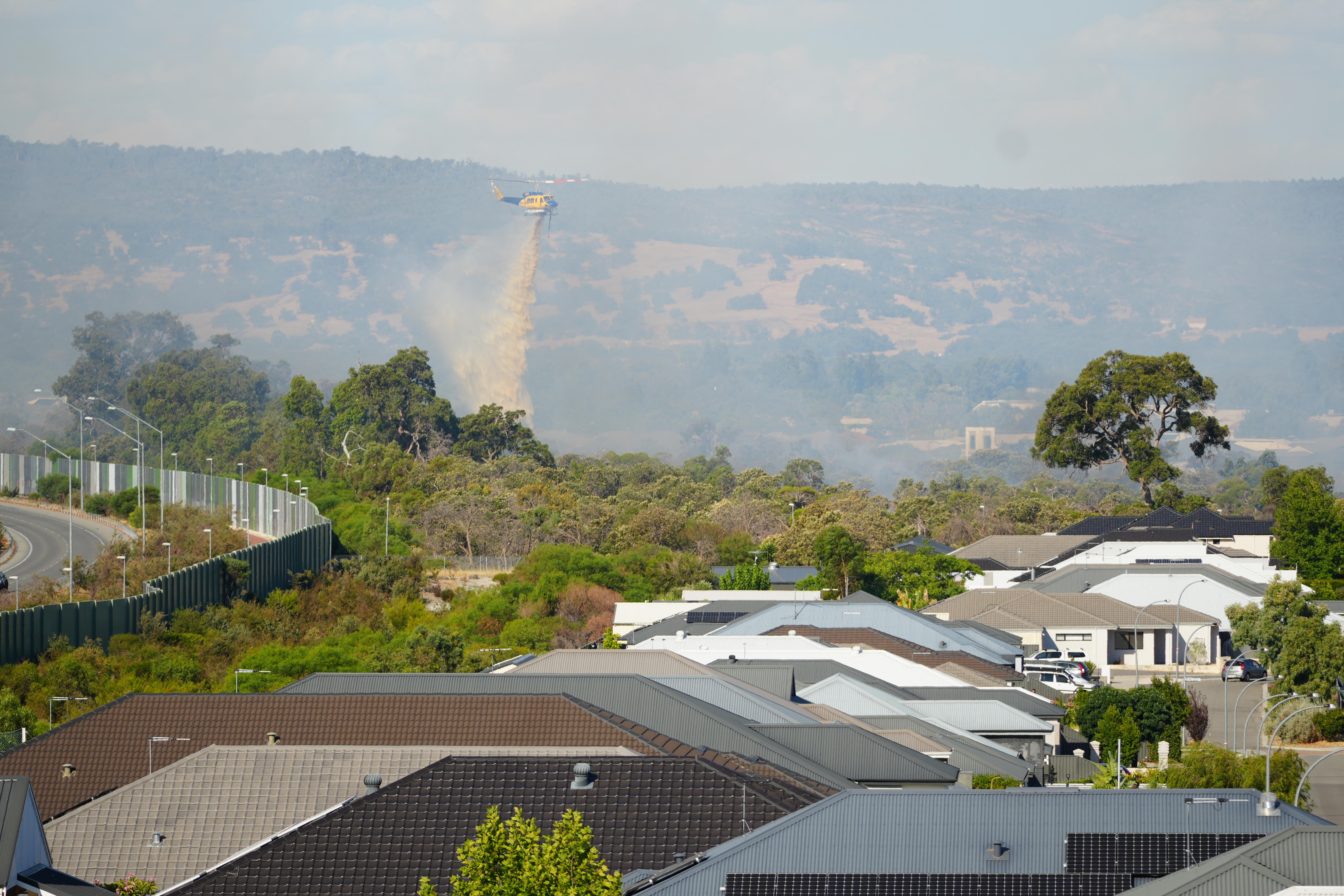 Helicóptero à distância bombardeando um incêndio em uma área residencial com água