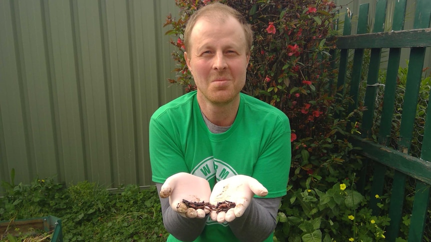 man with green shirt wears gloves in garden holding handful of worms