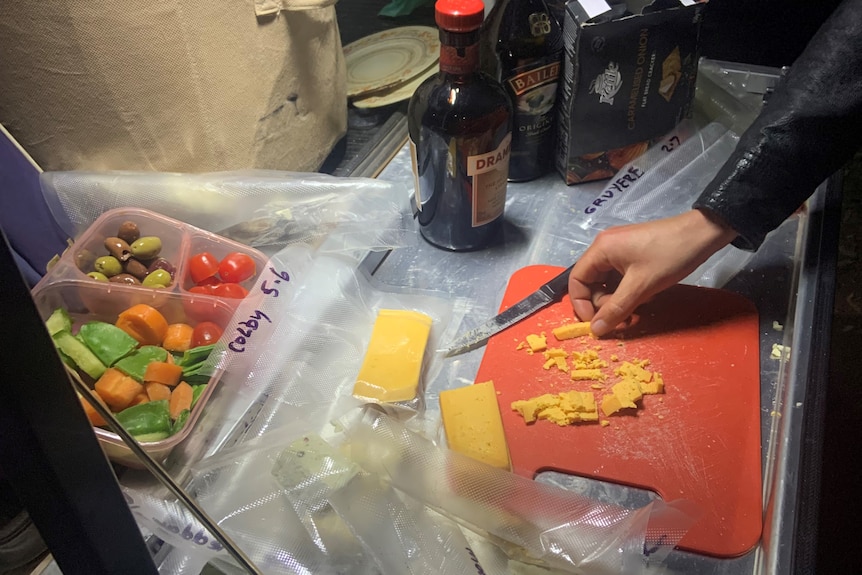 hand picking up a sample of cheese from a red cutting board with crudites and alcohol nearby 