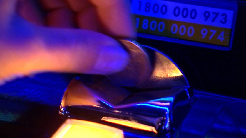 Close up of coins being slotted into a pokie machine.