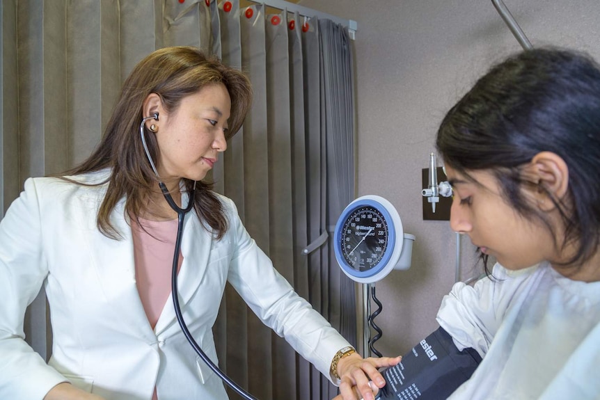 Alice Han checks the blood pressure of a patient in a hospital cubicle.