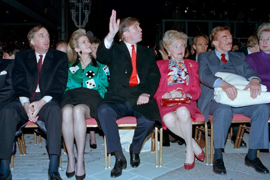 Robert Trump pictured sitting a few seats down from his brother Donald Trump, who is waving to staff members at an event.