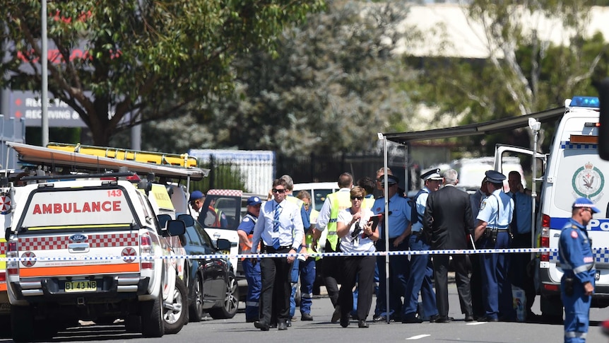 A large group of police gather behind police tape