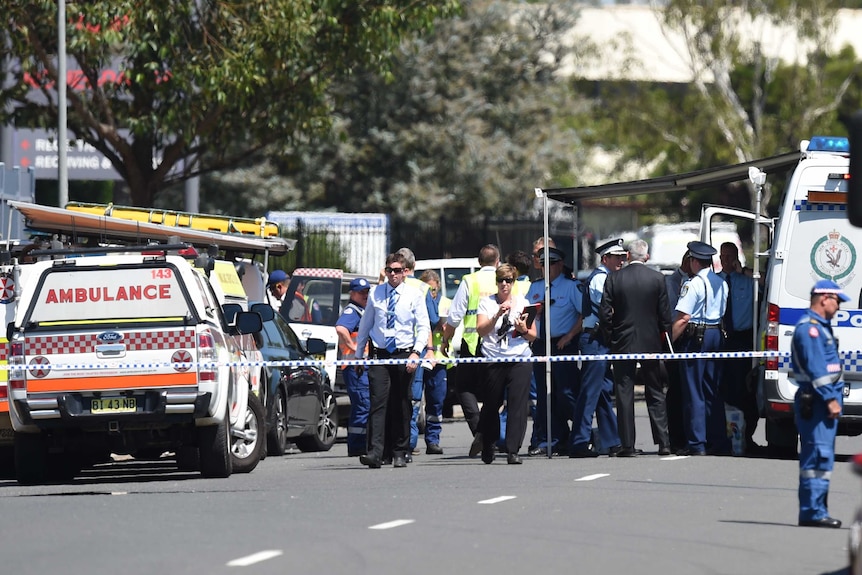 A large group of police gather behind police tape