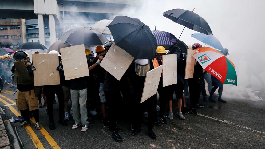 Demonstrators use shields and umbrellas