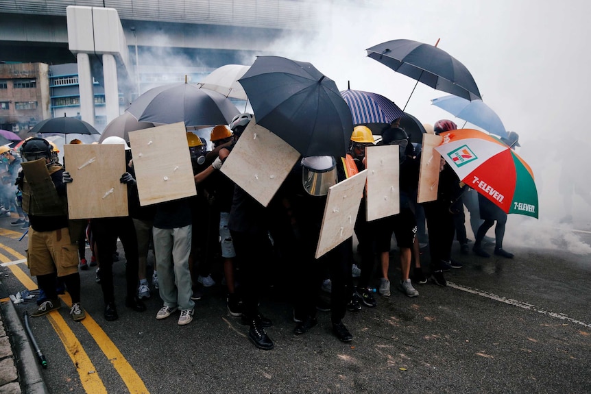 Demonstrators use shields and umbrellas