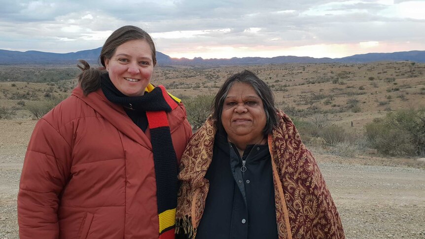 A younger Aboriginal woman and an Aboriginal elder wearing warm clothes and smiling in front of South Australian landscape.
