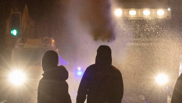 A group of protestors stand in front of a water cannon at night