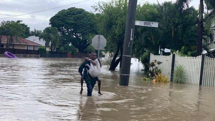 A man piggybacking someone on his back walks through the floods.