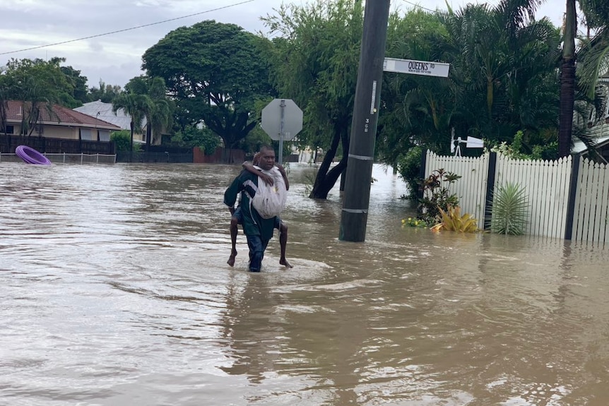 A man piggybacking someone on his back walks through the floods.