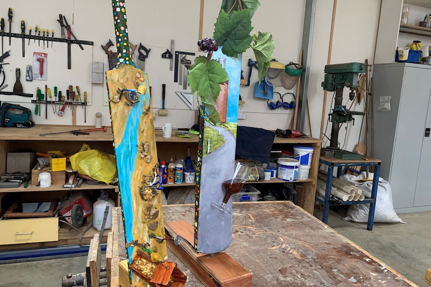 Two painted cricket bats sit upright on a work bench in a men's shed