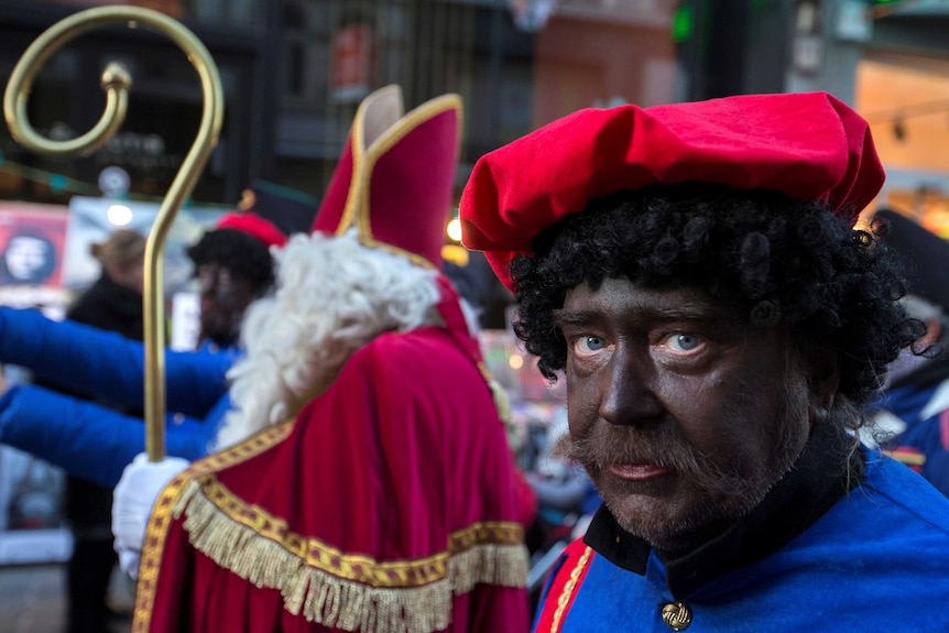 A man dressed as black pete stands with saint nicholas